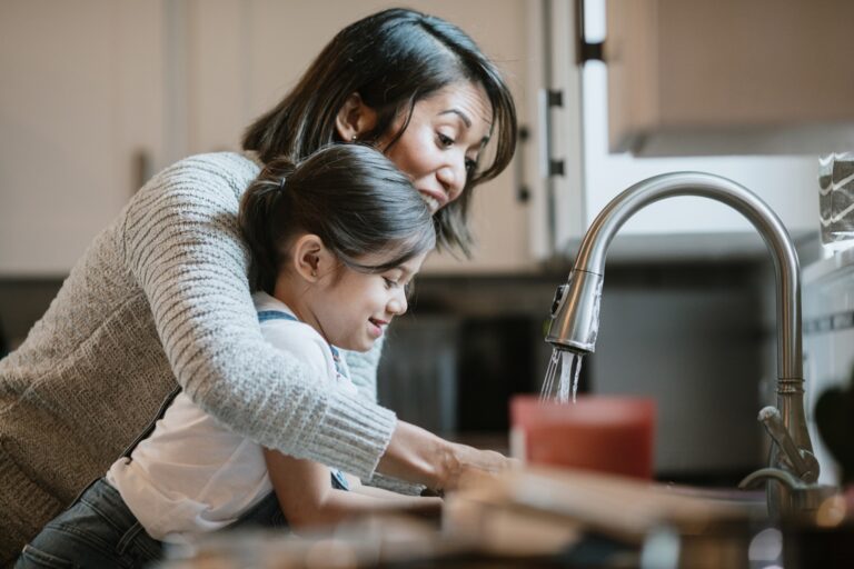 a woman and her daughter washing their hands on the faucet
